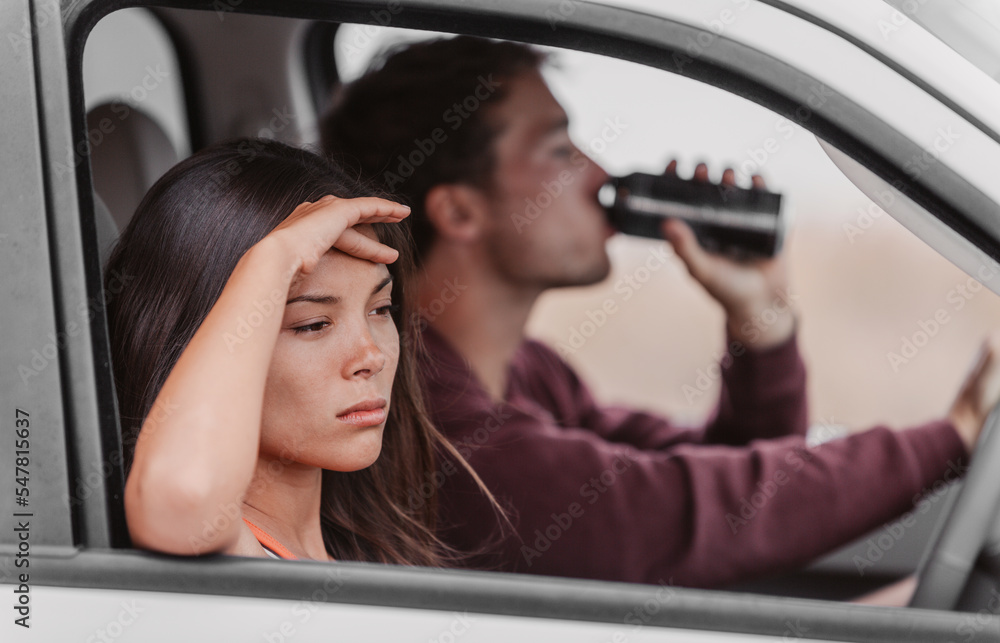 Drunk driving couple upset tired from drinking in car. Man driver holding beer beverage at the steering wheel, angry Asian woman girlfriend drowsy. Drunk driving couple upset tired from drinking in car. Man driver holding beer beverage at the steering wheel, angry Asian woman girlfriend drowsy.