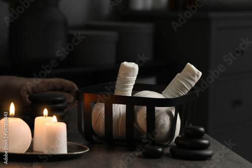 Herbal massage bags, burning candles and stones on grey table. Spa products
