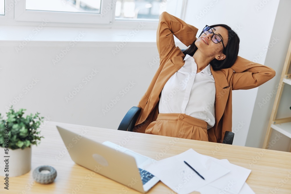 Business woman working in the office at a desk with a laptop, relaxing during a break with her hands behind her head and leaning back in her chair