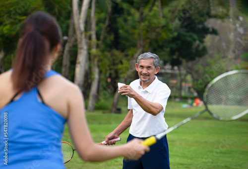 senior man and daughter playing badminton in the park,old man serving a shuttlecock to his daughter (focus at a man). concept elderly people lifestyle, health care, wellness,family relationship
