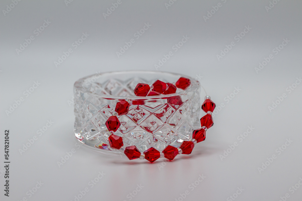 Macro abstract view of a small crystal bowl containing a string of red glass beads, with white background Macro abstract view of a small crystal bowl containing a string of red glass beads, with white background