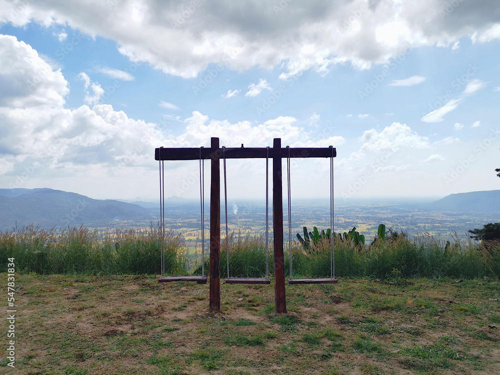 A wooden swing with 3 seats located on a large terrace on the mountain range.