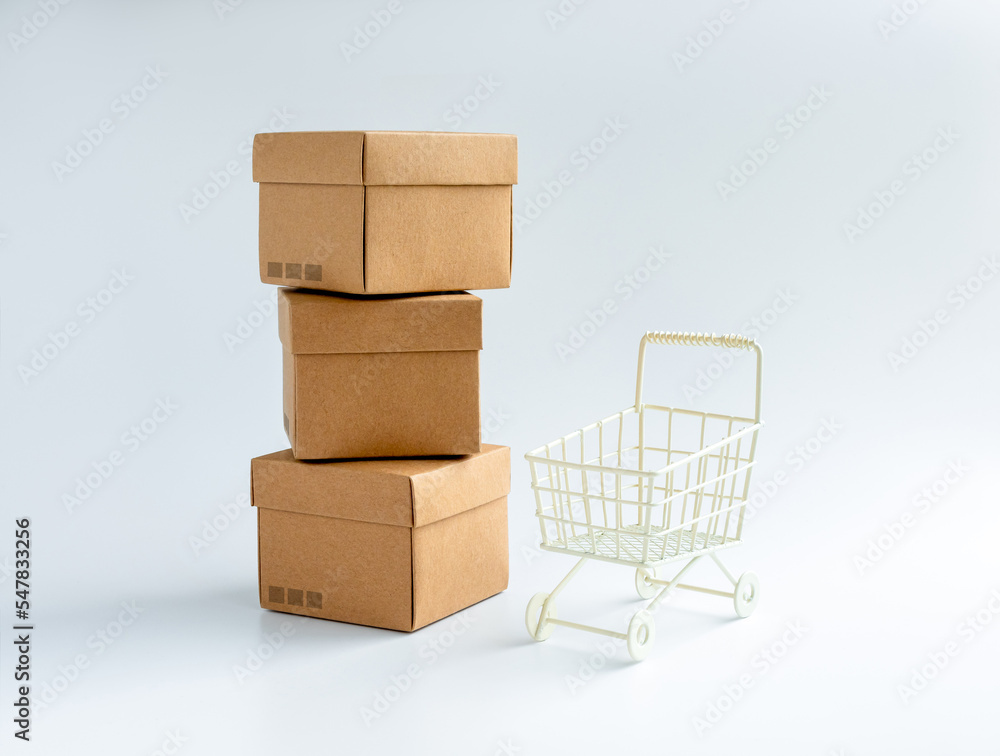 Cardboard parcel boxes stack and empty shopping trolley cart isolated on white background. Carton kraft paper box with lid on top. Delivery, cargo, package, online shopping and shipping concepts. Cardboard parcel boxes stack and empty shopping trolley cart isolated on white background. Carton kraft paper box with lid on top. Delivery, cargo, package, online shopping and shipping concepts.