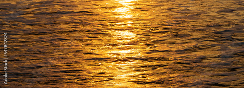 Gold sparkling sunrise on ocean water background. Bright abstract horizontal water texture banner. Copy space no people.