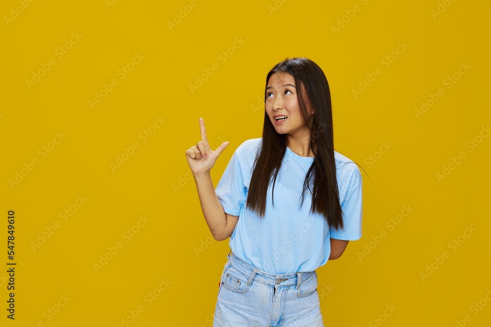 Asian woman smile with teeth hand gestures, signs and symbols on yellow background in blue t-shirt and jeans Asian woman smile with teeth hand gestures, signs and symbols on yellow background in blue t-shirt and jeans