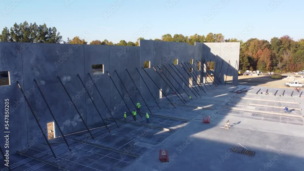 A long drone trucking shot of men securing support braces on concrete panels at a construction site.