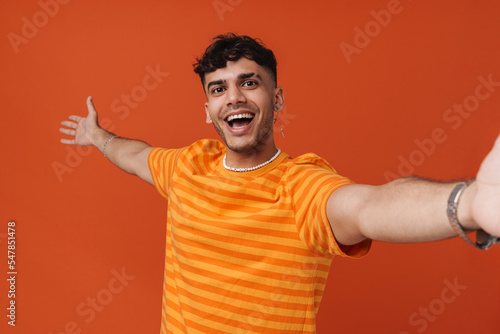 Brunette young man wearing t-shirt gesturing while taking selfie photo