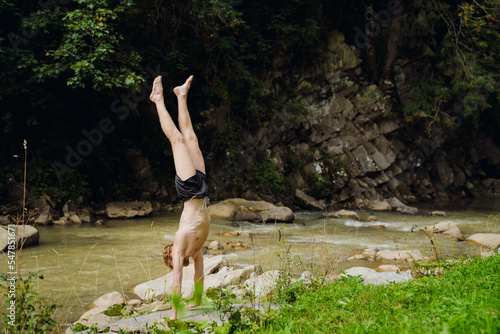 Fototapeta Naklejka Na Ścianę i Meble -  White young man wearing swimming trunks standing on his arms by river