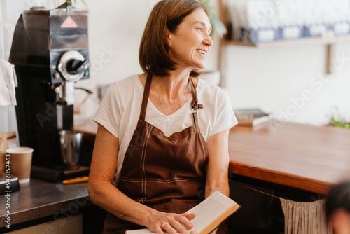 White mature barista woman reading book while working in cafe indoors