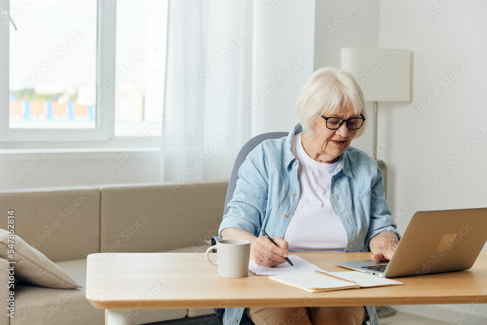 an attentive, responsible woman with gray hair, a pensioner, works from home at a laptop, carefully peering at the information on the monitor an attentive, responsible woman with gray hair, a pensioner, works from home at a laptop, carefully peering at the information on the monitor