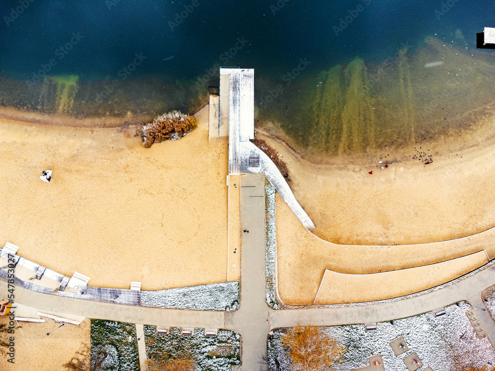 Aerial view of beautiful wooden pier, sea bay, sandy beach at winter. Aerial view of pier, transparent blue water. Frost and some snow. Pond, lake, Poland Bagry.