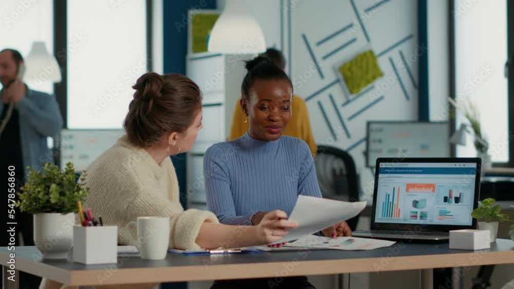 Startup employee working with african american coworker on group project comparing sales charts on clipboard with business papers on desk. Team of colleagues analzying market share looking at laptop. Startup employee working with african american coworker on group project comparing sales charts on clipboard with business papers on desk. Team of colleagues analzying market share looking at laptop.