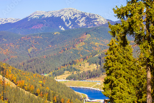 Beautiful postcard view from a top of a mountain on the mountains, cliffs, mountain range with orange, green trees. Autumn landscape of the Ukrainian Carpathians. Bukovel mountain lake with blue water