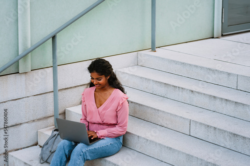 Young indian student woman working with laptop while sitting on stairs