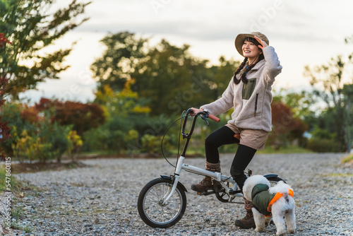 愛犬と秋冬のキャンプ場で自転車に乗ってサイクリングするアジア人女性
 #547860815