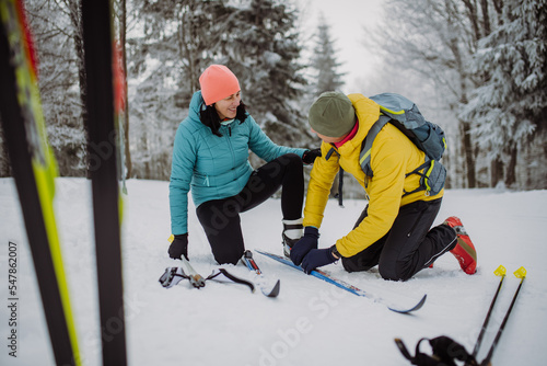 Senior couple putting on skis, preparing for ride in winter snowy nature.