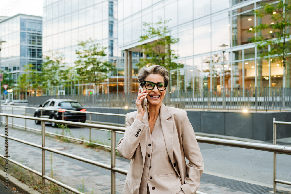 Mature grey woman talking on cellphone while standing on city street