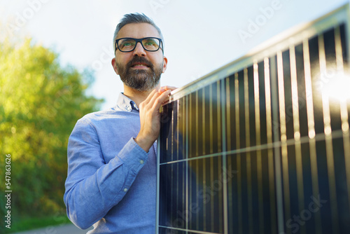 Businessman holding solar panel, standing outdoor at garden.