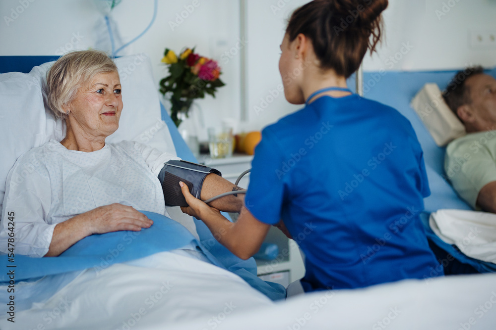 Obraz premium Young nurse chcecking blood presure to senior patient.