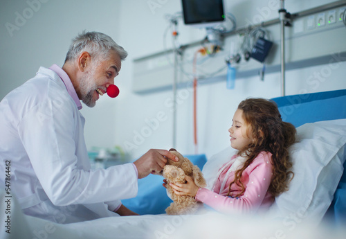 Fotografie, Obraz Happy doctor with clown red nose taking care and playing with little girl
