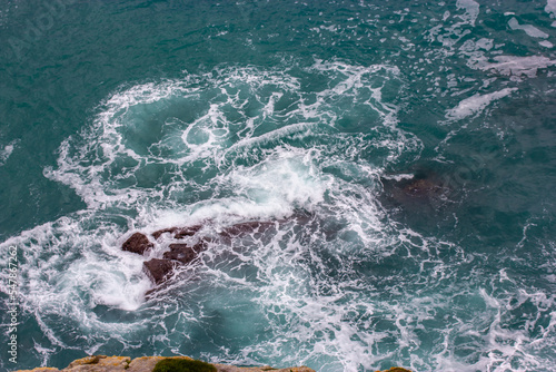 A raging ocean with a funnel, vortex of blue water viewed from a cliff. Circulating water top view. Rocks visible from under water, rocky Atlantic coastline. Aquatic background, wallpaper. Nature.