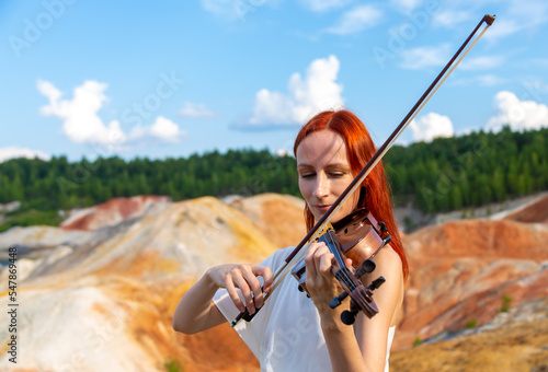 a red-haired violinist plays in nature and smiles close up portrait