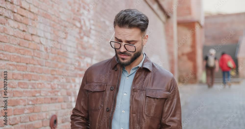 sexy young fashion man looking around, adjusting brown leather jacket and rubbing palms while walking outside in a medieval town from Romania sexy young fashion man looking around, adjusting brown leather jacket and rubbing palms while walking outside in a medieval town from Romania