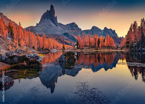 Huge mountain peak reflected in the calm waters of Federa lake. Spectacular sunrise in Dolomite Alps with orange larch trees on the shore. Colorful morning scene of Italy, Europe.