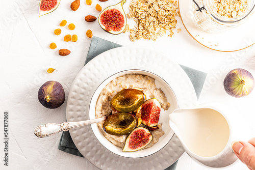 delicious healthy breakfast. a woman's hand pours milk into oatmeal with fruit. a bowl of freshly made oatmeal. top view. white background.