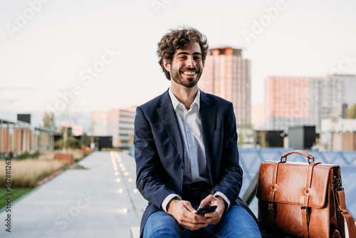 Happy businessman sitting by briefcase on railing photo