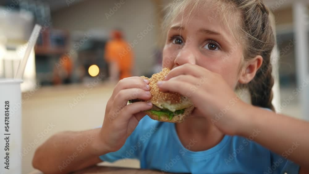 child kid eating a burger in a cafe. fast food nutrition health concept. daughter girl eats with pleasure lifestyle hamburger. a little schoolgirl has a snack in a cafe with a burger sandwich