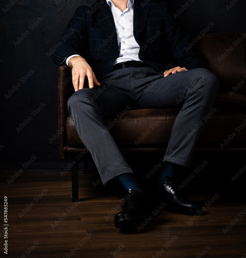 Unrecognizable stylish macho man sits relaxed on the sofa in the dark. Unrecognizable stylish macho man sits relaxed on the sofa in the dark.