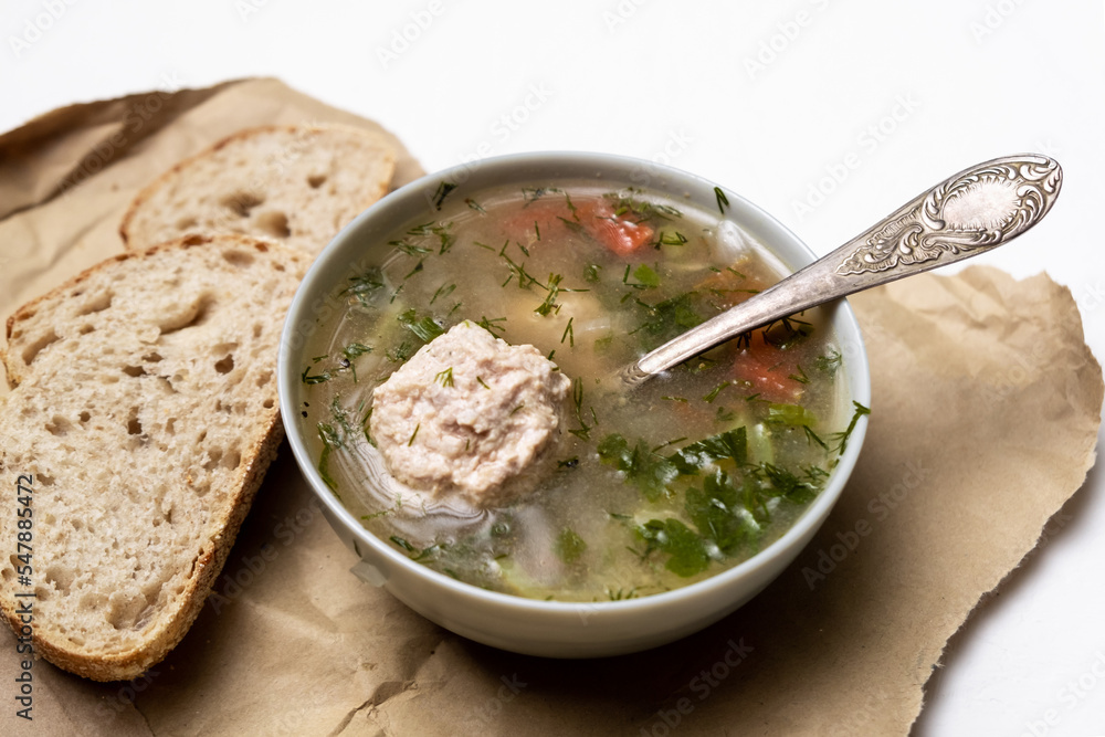 Vegetable soup with meatballs in a plate on a white background. Two slices of bread side by side. Vegetable soup with meatballs in a plate on a white background. Two slices of bread side by side.