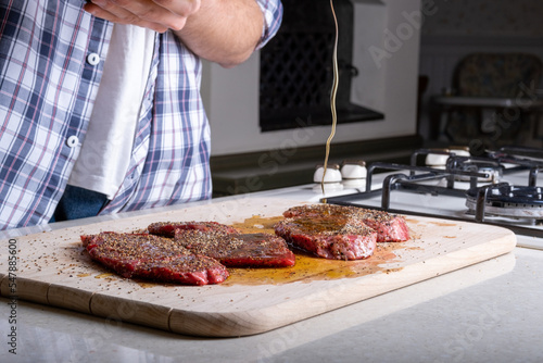 A man prepares a juicy pepper steak. Add extra virgin olive oil to pepper steak. Marinade for steak