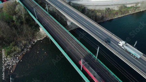 A Passenger train crossing a river via a railroad bridge located next to a highway where trucks drive next to it. Filmed with a drone slowly turning and panning. photo