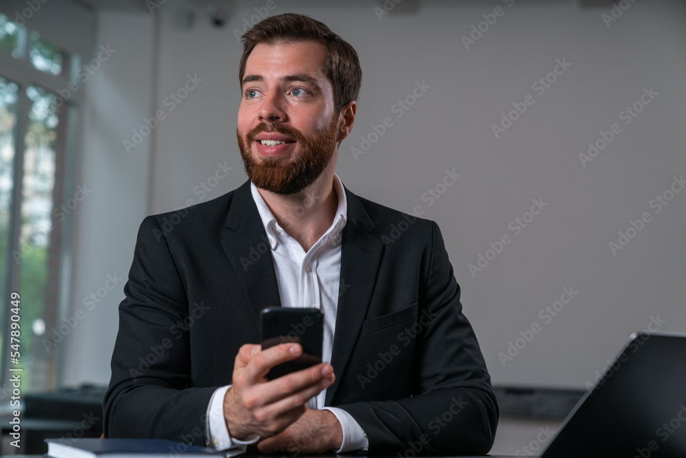 Glad handsome businessman wearing formal suit watching away holding smartphone Glad handsome businessman wearing formal suit watching away holding smartphone