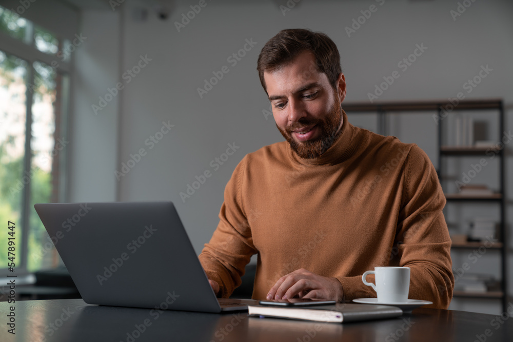 Smiling businessman in casual wear working on laptop at office Smiling businessman in casual wear working on laptop at office