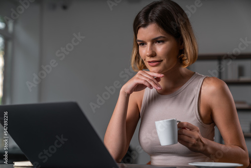 Anxious businesswoman working on laptop drinking coffee touching chin