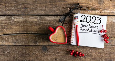 New year resolutions 2023 on desk. 2023 resolutions list with notebook, coffee cup, decorations on table. Goals, resolutions, plan, action concept. New Year 2023 background. Copy space