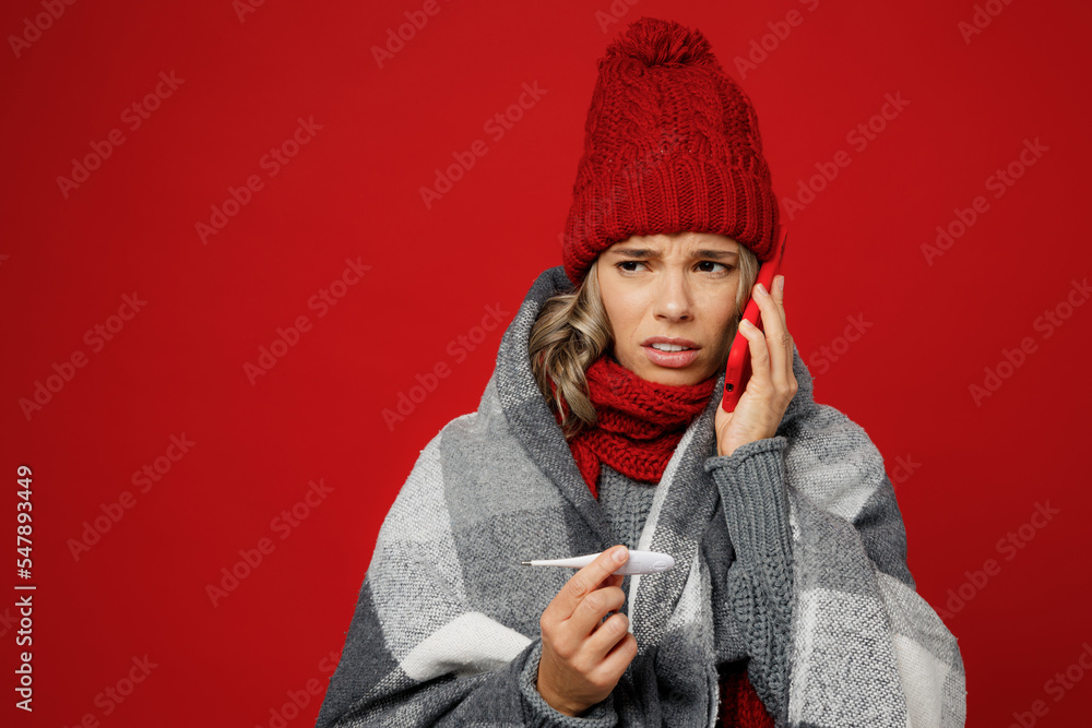 Young woman in scarf hat grey plaid hold thermometer in mouth talk speak on mobile cell phone isolated on plain red background studio Healthy lifestyle ill sick disease treatment cold season concept Young woman in scarf hat grey plaid hold thermometer in mouth talk speak on mobile cell phone isolated on plain red background studio Healthy lifestyle ill sick disease treatment cold season concept