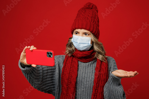 Young woman in grey sweater scarf hat mask talk video call mobile cell phone spread hand isolated on plain red background Healthy lifestyle ill sick disease treatment cold season coronavirus concept photo