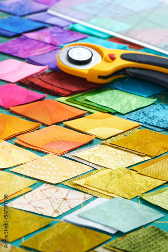 Pile of colorful fabric diamonds on cutter mat, quilting accessories