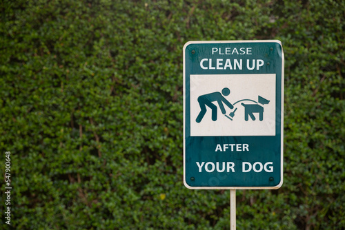 Clean Up After Your Dog sign against green grass in park .
