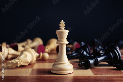 White king among fallen chess pieces on chessboard against black background, closeup. Competition concept