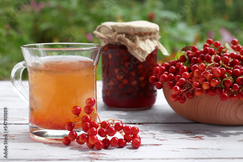 Cup of tea, jam and ripe viburnum berries on white wooden table outdoors