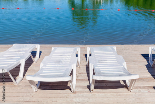 Vacant white sun loungers stand on wooden pier