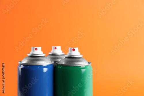 Colorful cans of spray paints on orange background, closeup. Space for text