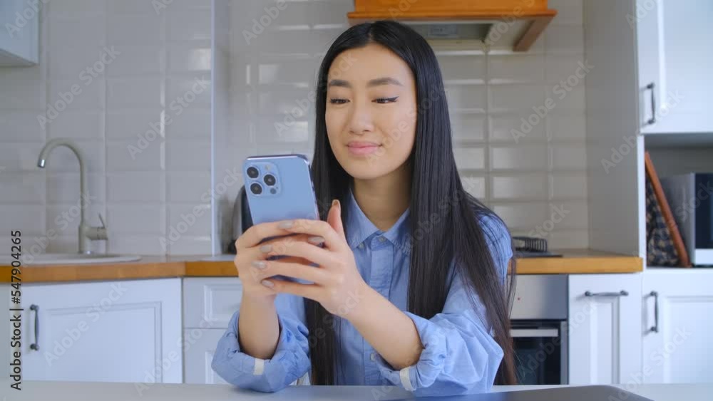 Cheerful Vietnamese girl browsing mobile app on smartphone. Happy Asian female using modern blue cellphone for communication 
