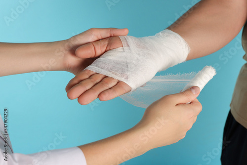 Doctor applying bandage onto patient's hand on light blue background, closeup