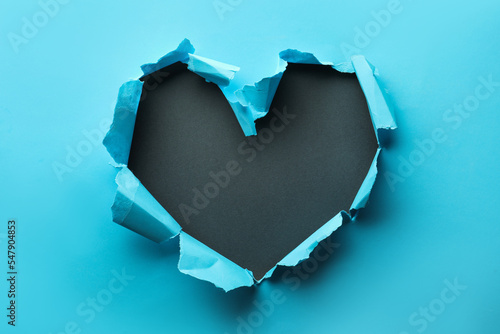 Torn heart shaped hole in light blue paper on black background